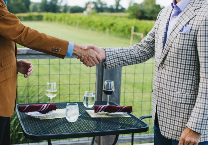 Two local business owners shaking hands over a meal on the balcony of our primary dining space at Farmer and Frenchman Winery.