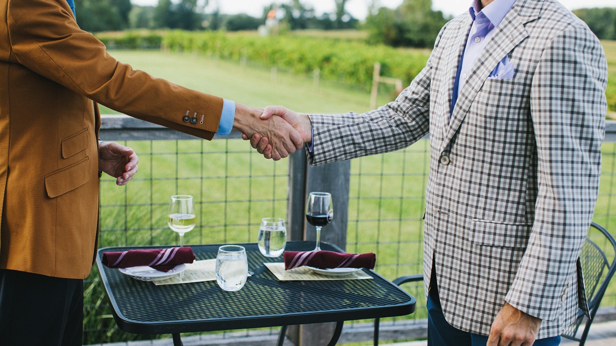 Two local business owners shaking hands over a meal on the balcony of our primary dining space at Farmer and Frenchman Winery.